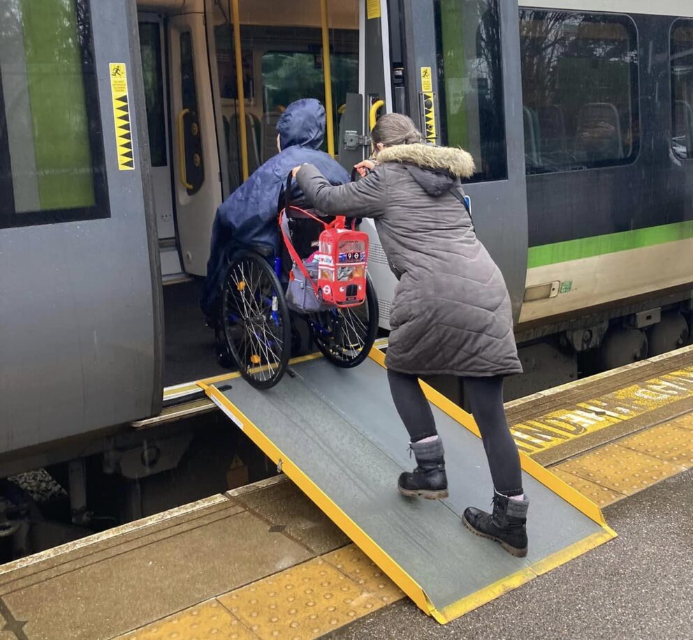 Young person in wheel chair being wheeled up a very steep ramp, onto a train