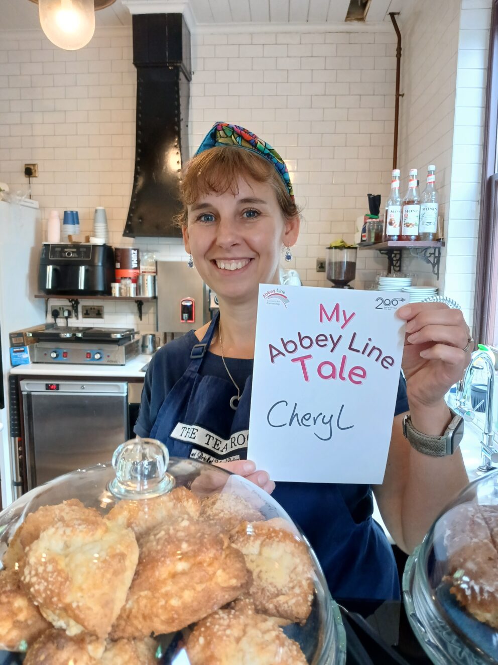 A cafe manager smiling holding up a sign in a cafe kitchen
